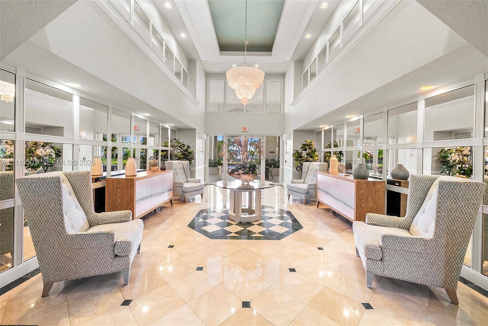 Double-height entryway featuring a tray ceiling, ornate tiered chandelier, polished stone flooring with geometric tile inlay, and floor-to-ceiling wall mirrors
