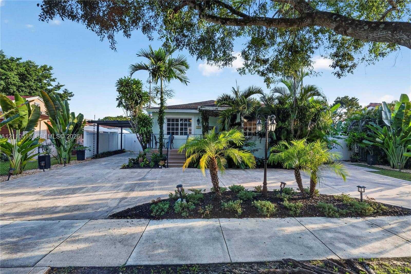6520 SW 16th Terrace, West Miami, FL 33155 Exterior facade featuring a covered entryway, paved driveway, carport, and landscape elements including palm trees and mulched garden beds