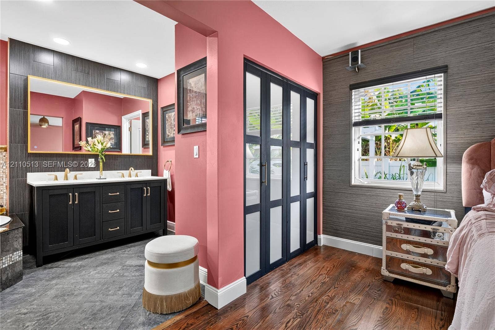 6520 SW 16th Terrace, West Miami, FL 33155 Double vanity featuring a white countertop and gold-toned hardware, large rectangular wall mirror, wood-finish flooring, dark-toned textured wall treatment, and floor-to-ceiling glass-paneled closet doors