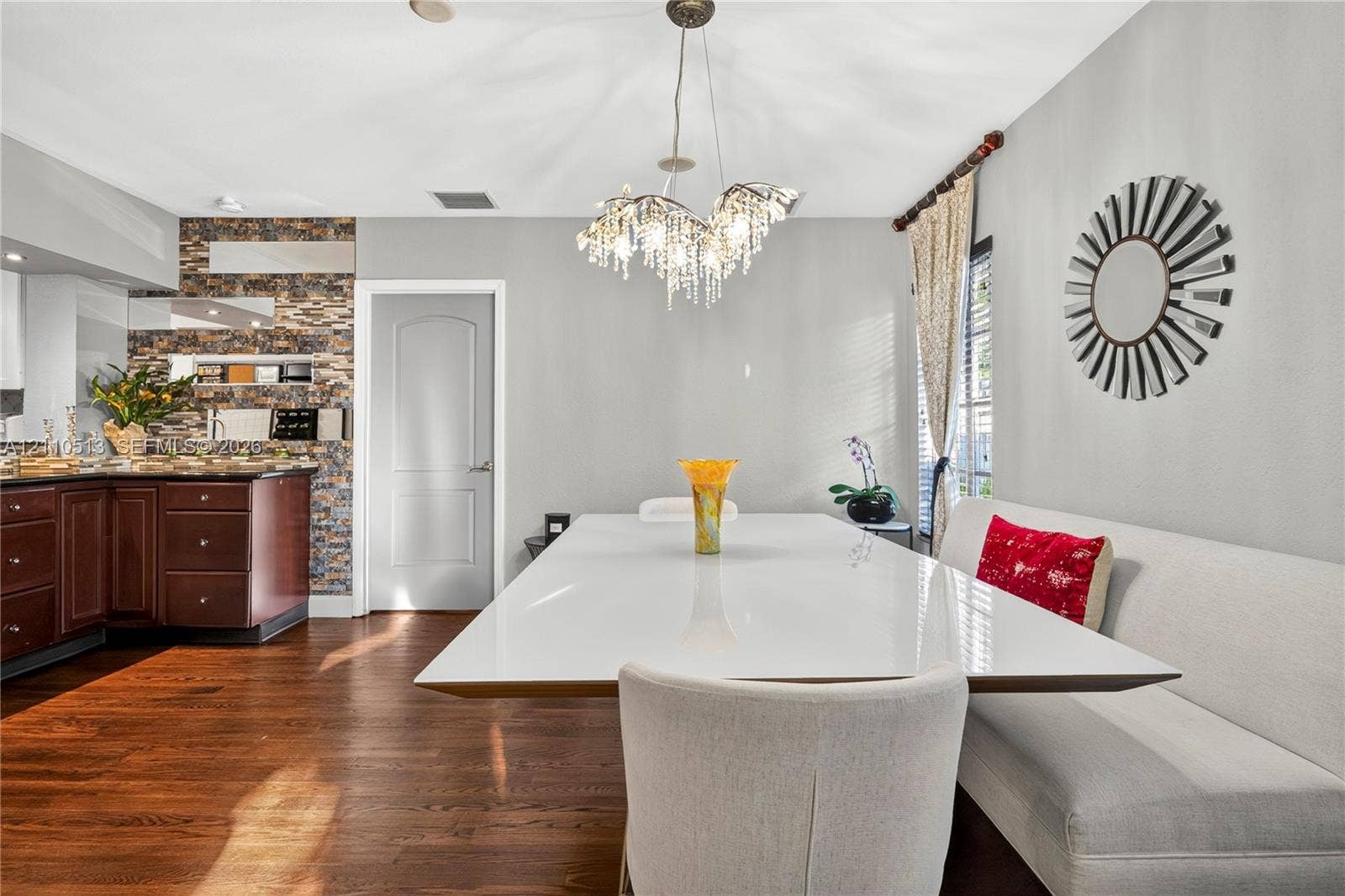 6520 SW 16th Terrace, West Miami, FL 33155 Dining area featuring wood-finish flooring, a tiered crystal chandelier, an intricate stacked-stone accent wall, and cabinetry with dark-toned finishes