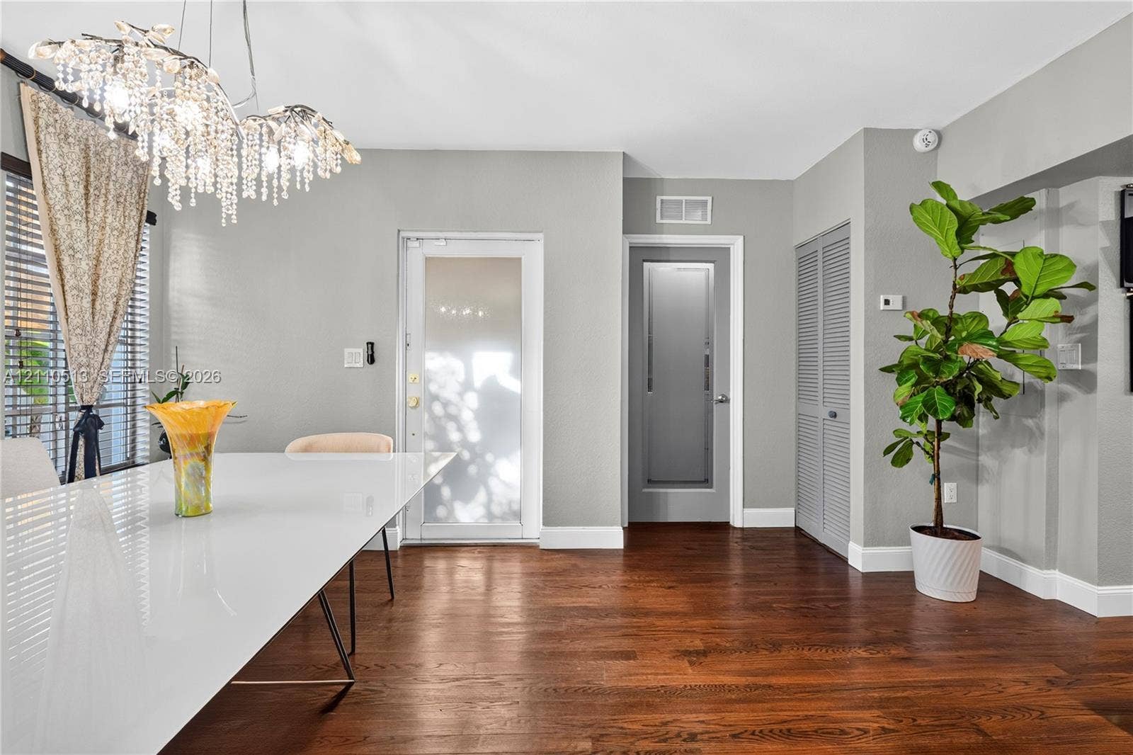 6520 SW 16th Terrace, West Miami, FL 33155 Interior space featuring wood-finish flooring, a multi-tiered crystal chandelier, a glass-panel exterior door, and louvered-style closet doors