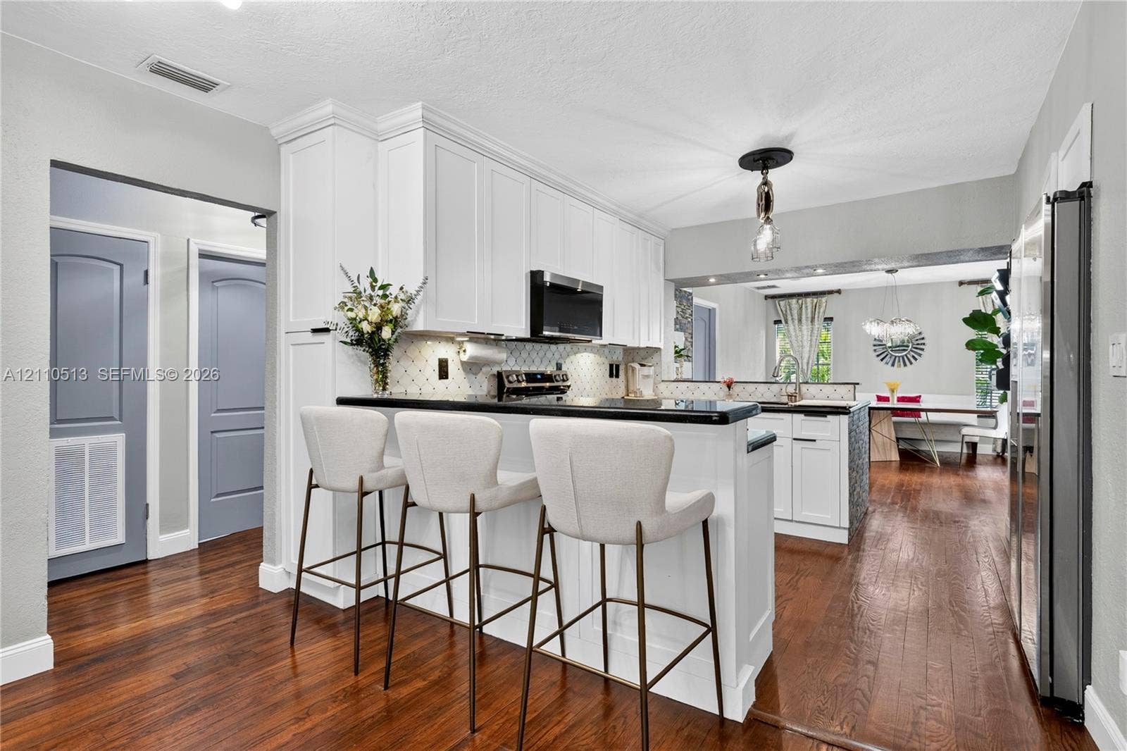 6520 SW 16th Terrace, West Miami, FL 33155 Kitchen featuring white shaker-style cabinetry, dark stone countertops, wood-finish flooring, a breakfast bar, and a decorative tile backsplash