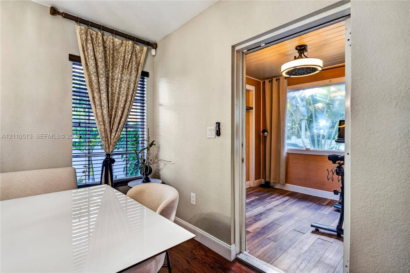6520 SW 16th Terrace, West Miami, FL 33155 Interior space featuring wood-finish flooring, horizontal window blinds, a tiered ceiling light fixture, and wood-paneled wall accents