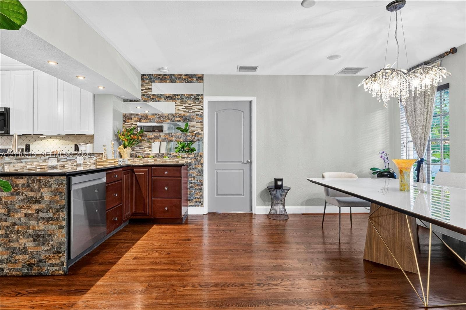 6520 SW 16th Terrace, West Miami, FL 33155 Kitchen featuring a stone-clad breakfast bar, dark wood cabinetry, white upper cabinets, wood-finish flooring, and a crystal chandelier