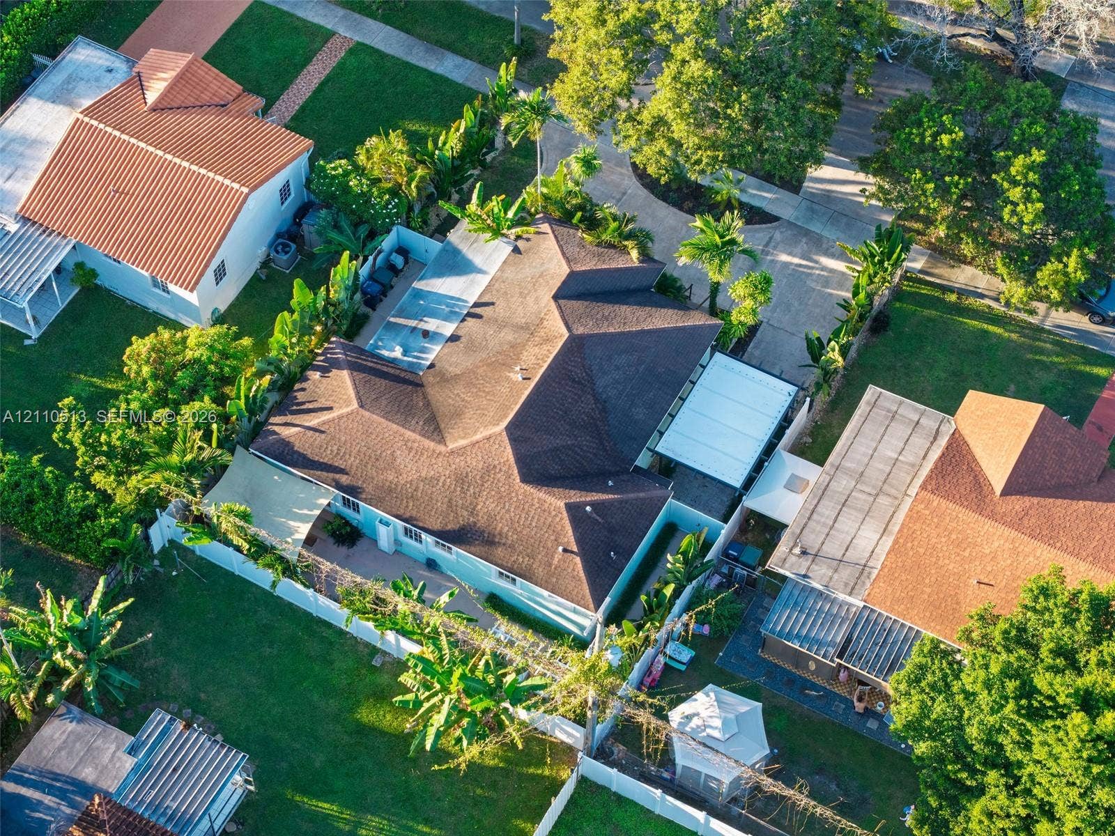 6520 SW 16th Terrace, West Miami, FL 33155 Aerial perspective of a property featuring an asphalt shingle roof, a concrete driveway, a screened-in swimming pool enclosure, and lush tropical landscaping