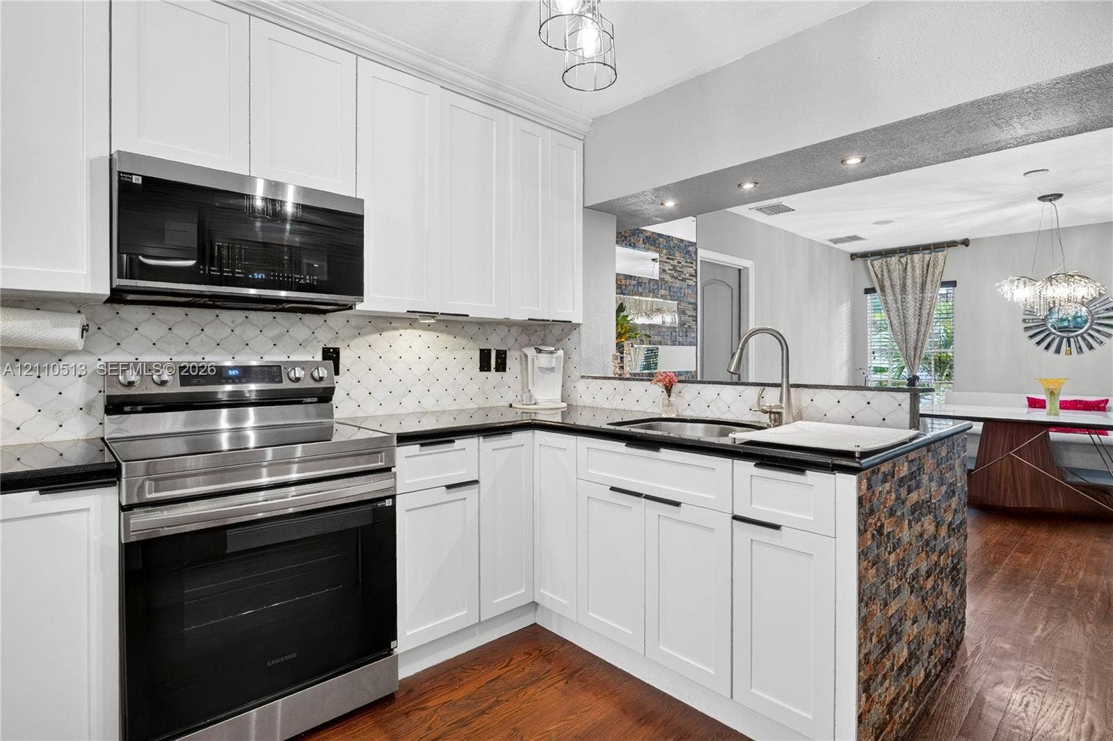 6520 SW 16th Terrace, West Miami, FL 33155 Modern kitchen featuring white shaker cabinetry, stainless steel appliances including a double wall oven, black quartz countertops, a decorative tile backsplash, and a large island with wood-tone base