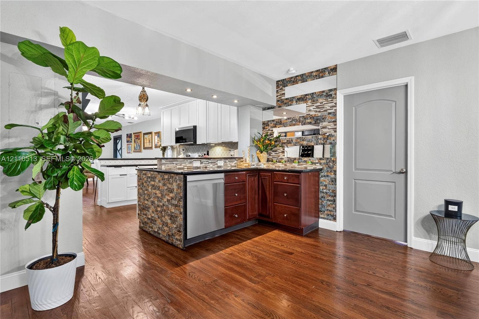 6520 SW 16th Terrace, West Miami, FL 33155 Kitchen featuring wood-finish flooring, a tiered center island with stone-veneer facing, stainless steel dishwasher, and a stone-veneer accent wall