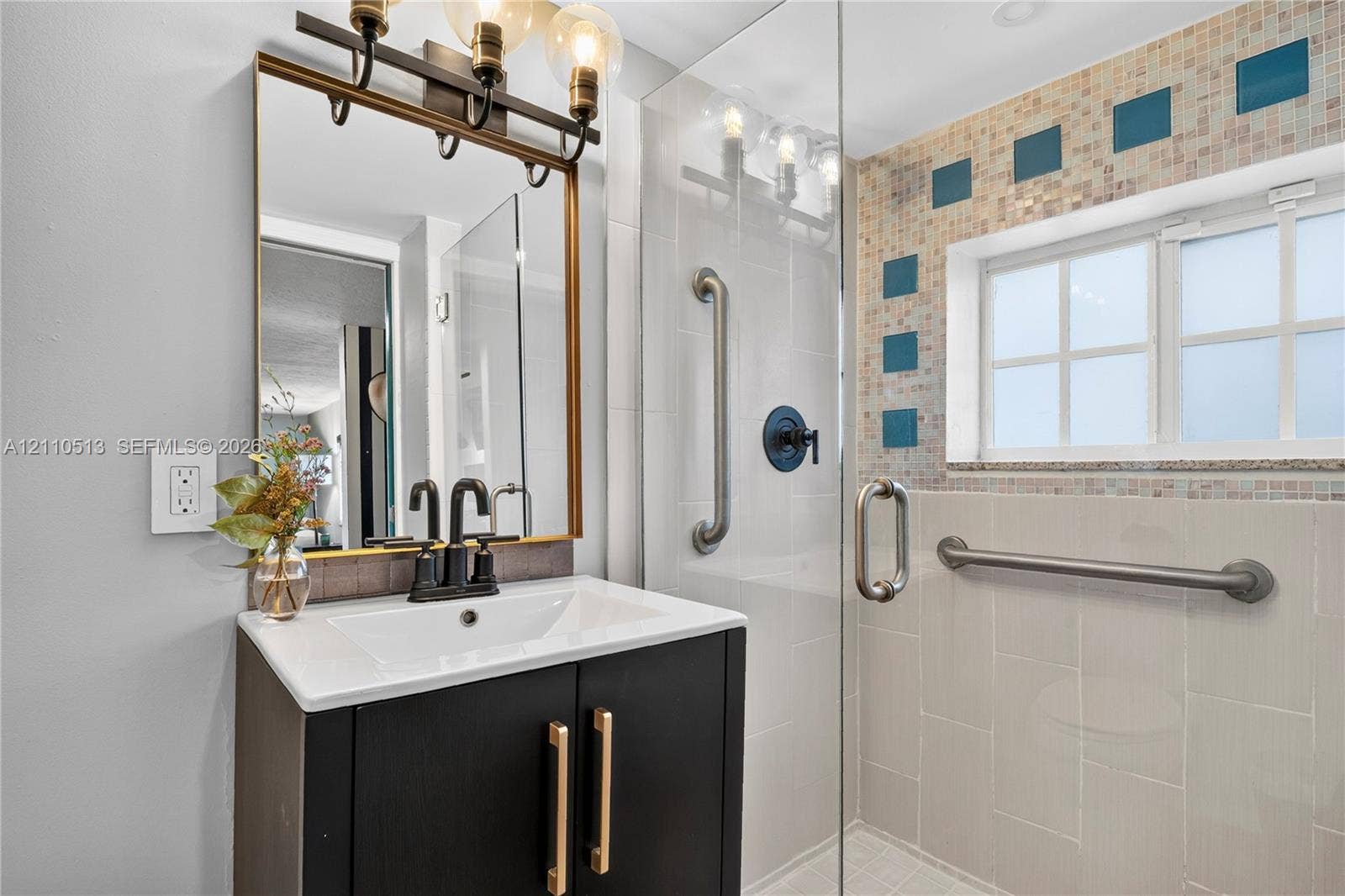 6520 SW 16th Terrace, West Miami, FL 33155 Dark cabinetry vanity with a white countertop, metallic hardware, rectangular framed mirror with integrated light fixture, and glass-enclosed shower with tiled accents