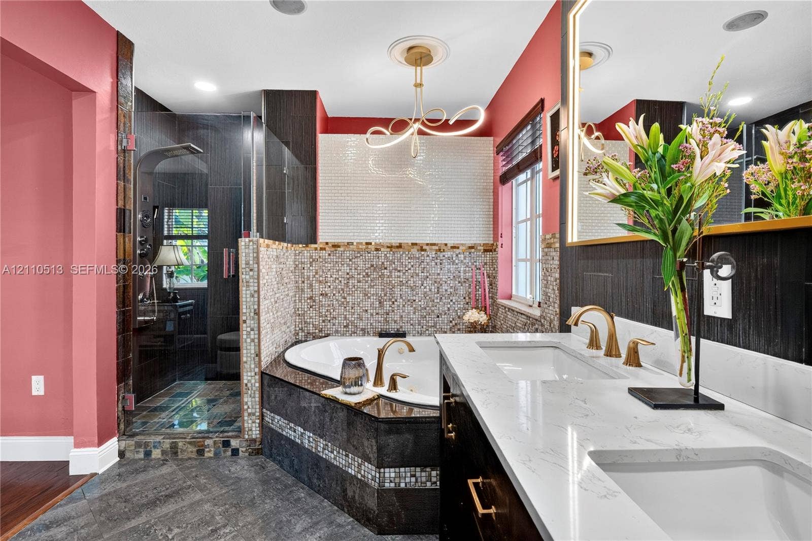 6520 SW 16th Terrace, West Miami, FL 33155 Bathroom featuring a dual-sink vanity with white stone-finish countertops, gold-toned fixtures, a corner jetted soaking tub with mosaic tile surround, and an enclosed shower with dark tile walls