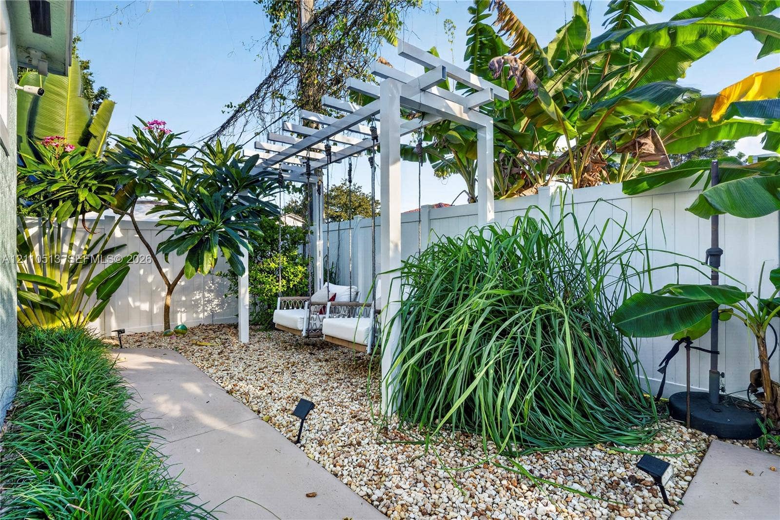 6520 SW 16th Terrace, West Miami, FL 33155 Custom white wooden pergola, gravel landscaping, concrete pathway, mature tropical vegetation, and perimeter vinyl fencing