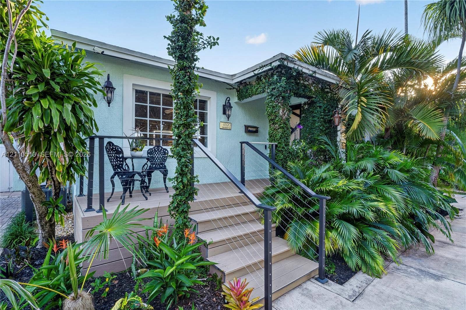 6520 SW 16th Terrace, West Miami, FL 33155 Exterior featuring light-colored stucco siding, raised composite decking, metal cable railings, and established landscaping