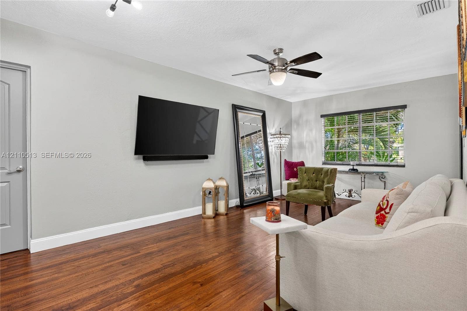 6520 SW 16th Terrace, West Miami, FL 33155 Living area featuring wood-finish flooring, a multi-blade ceiling fan with integrated light fixture, a paneled door, and a horizontal window with grid detail