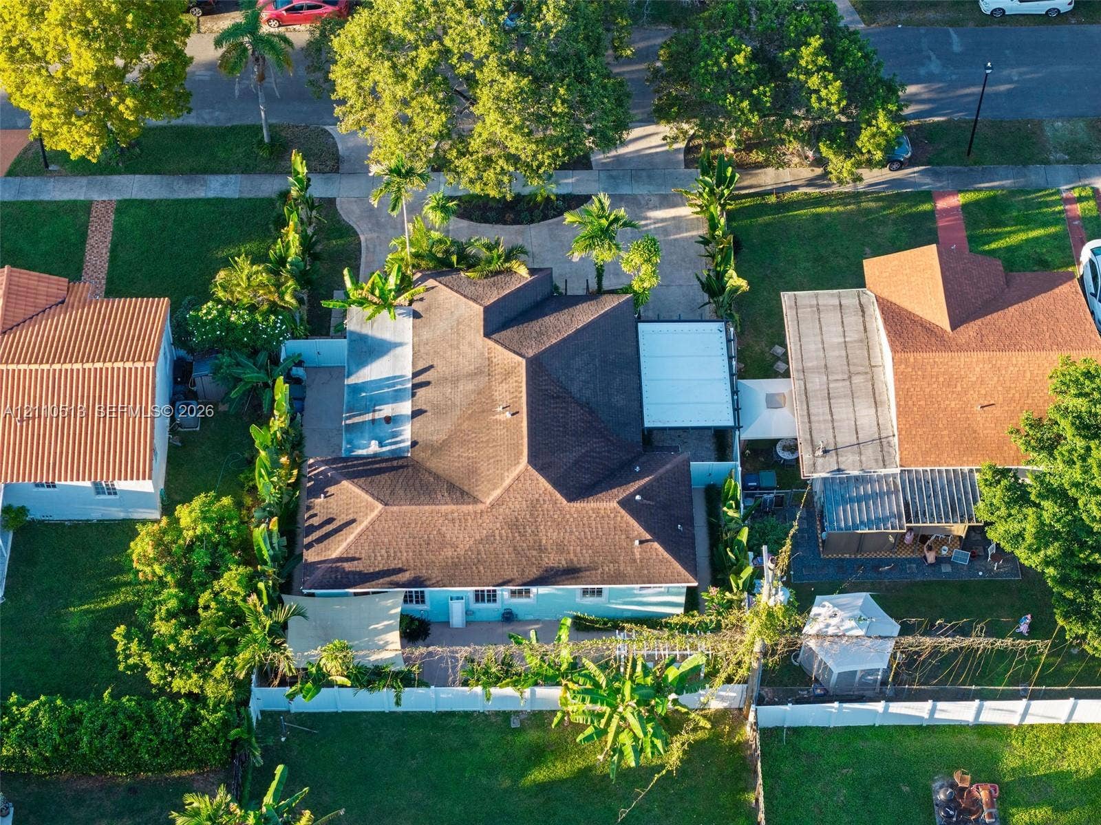 6520 SW 16th Terrace, West Miami, FL 33155 Aerial perspective featuring a multi-hipped roofline, paved driveway, covered patio area, white vinyl perimeter fencing, and mature landscaping