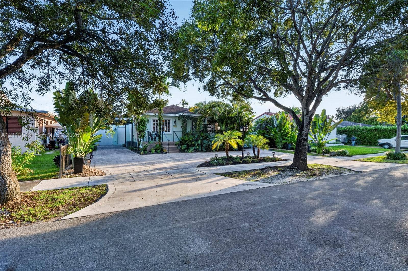 6520 SW 16th Terrace, West Miami, FL 33155 Exterior featuring a concrete driveway, mature canopy trees, lush tropical landscaping, and a raised front entryway