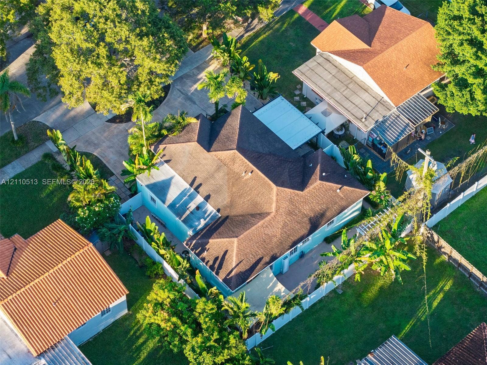 6520 SW 16th Terrace, West Miami, FL 33155 Aerial perspective of a property featuring a multi-pitched shingled roof, a paved driveway, and mature landscaping enclosed by white perimeter fencing