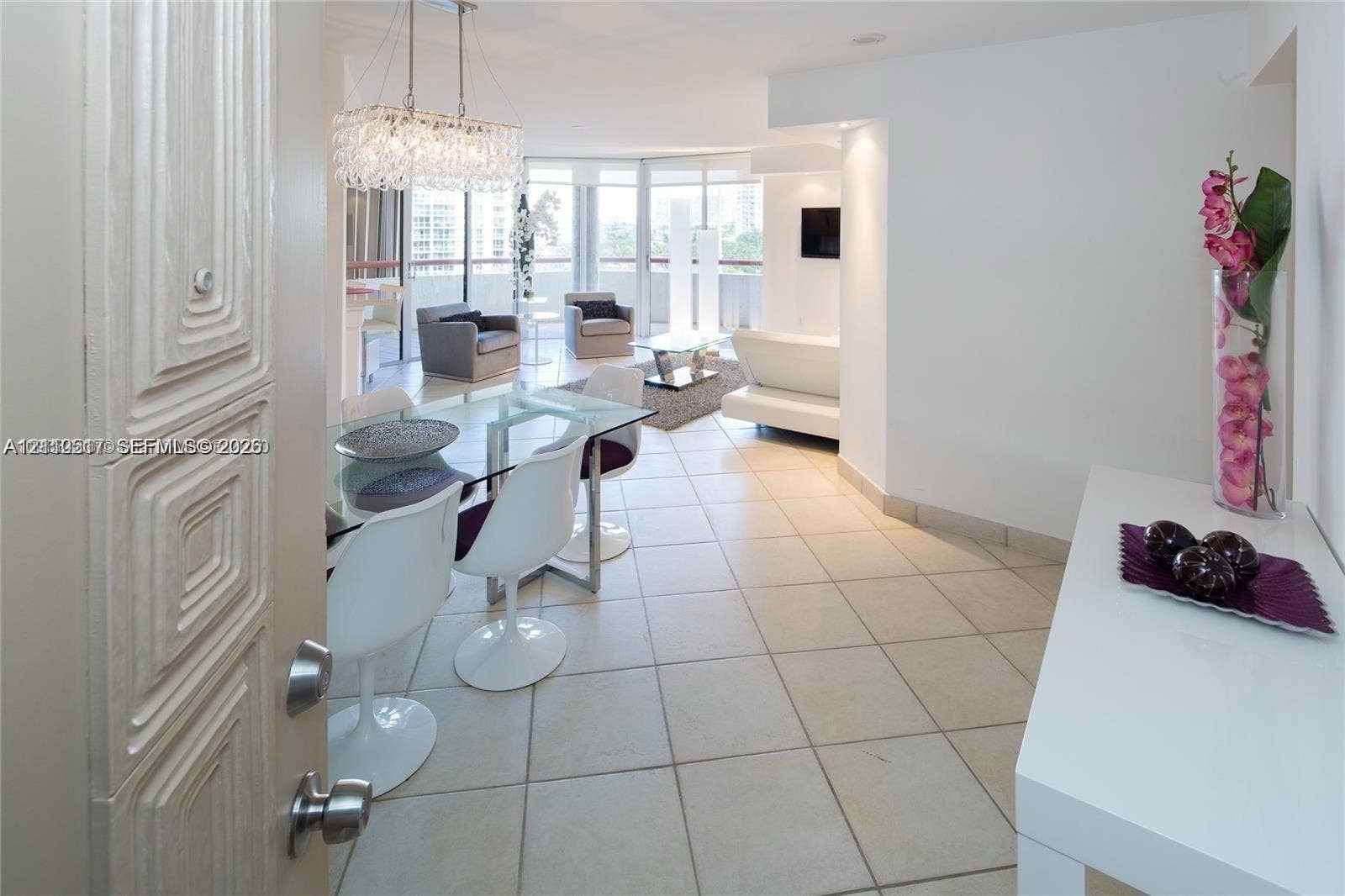 Large-format tile flooring, crystal-accented chandelier, and floor-to-ceiling glass paneling featuring balcony access