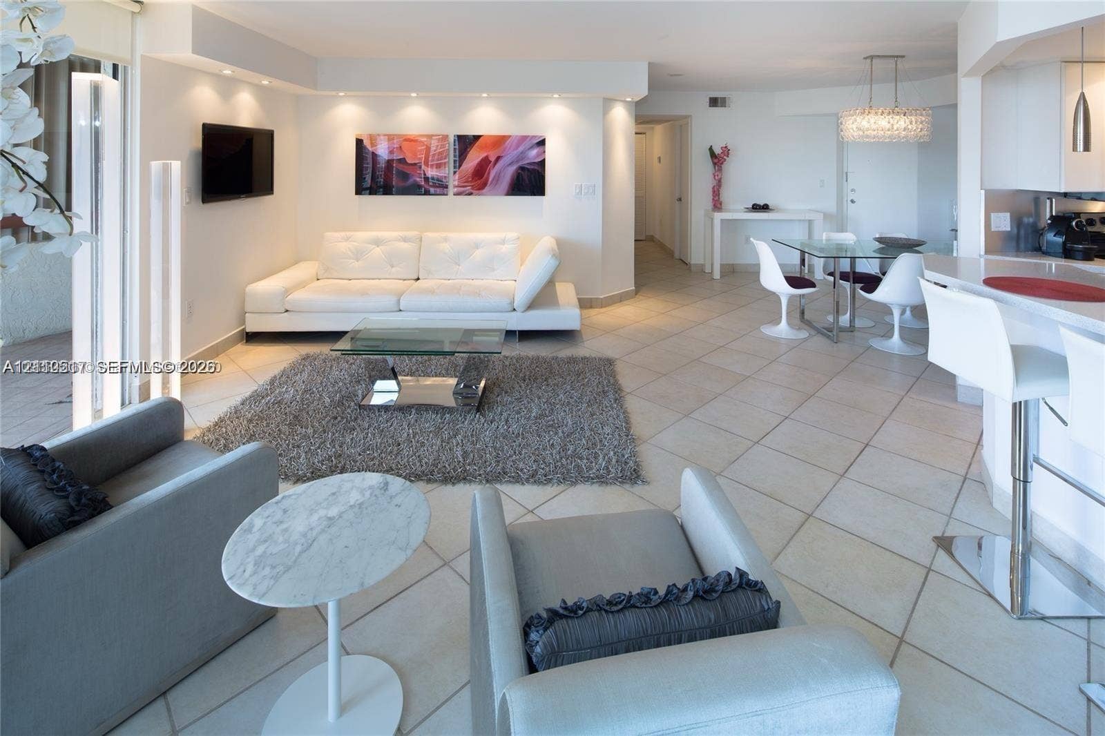 Open concept living area featuring large-format ceramic tile flooring, recessed ceiling lighting, a breakfast bar with stone-finish countertop, and a tiered crystal chandelier