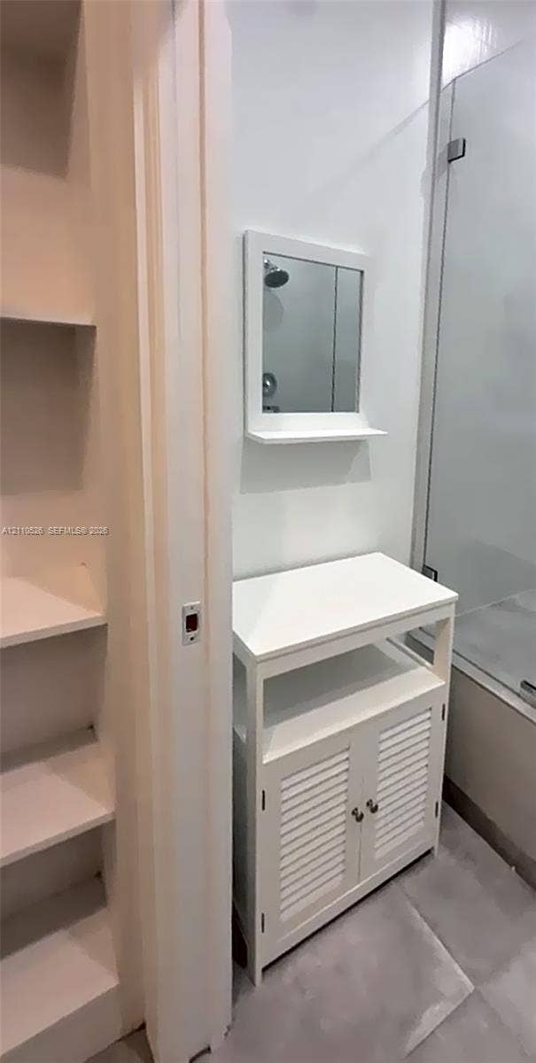 15677 SW 20 Street, #B, Miami, Miami, FL 33185 White vanity with louvered cabinet doors, open shelving, and integrated mirror, accompanied by built-in wall shelving and a glass-enclosed shower