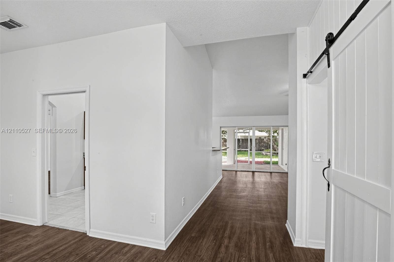 5509 NW Commodore Terrace, Port St Lucie, FL 34983 Interior featuring white vertical-plank sliding barn door, wood-finish flooring, vaulted ceilings, and multi-panel sliding glass doors