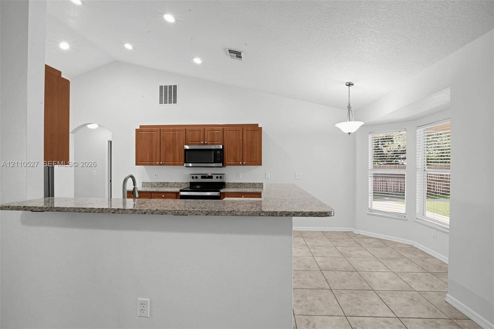 5509 NW Commodore Terrace, Port St Lucie, FL 34983 Kitchen featuring a stone-look countertop, wood cabinetry, recessed lighting, tile flooring, and vaulted ceilings