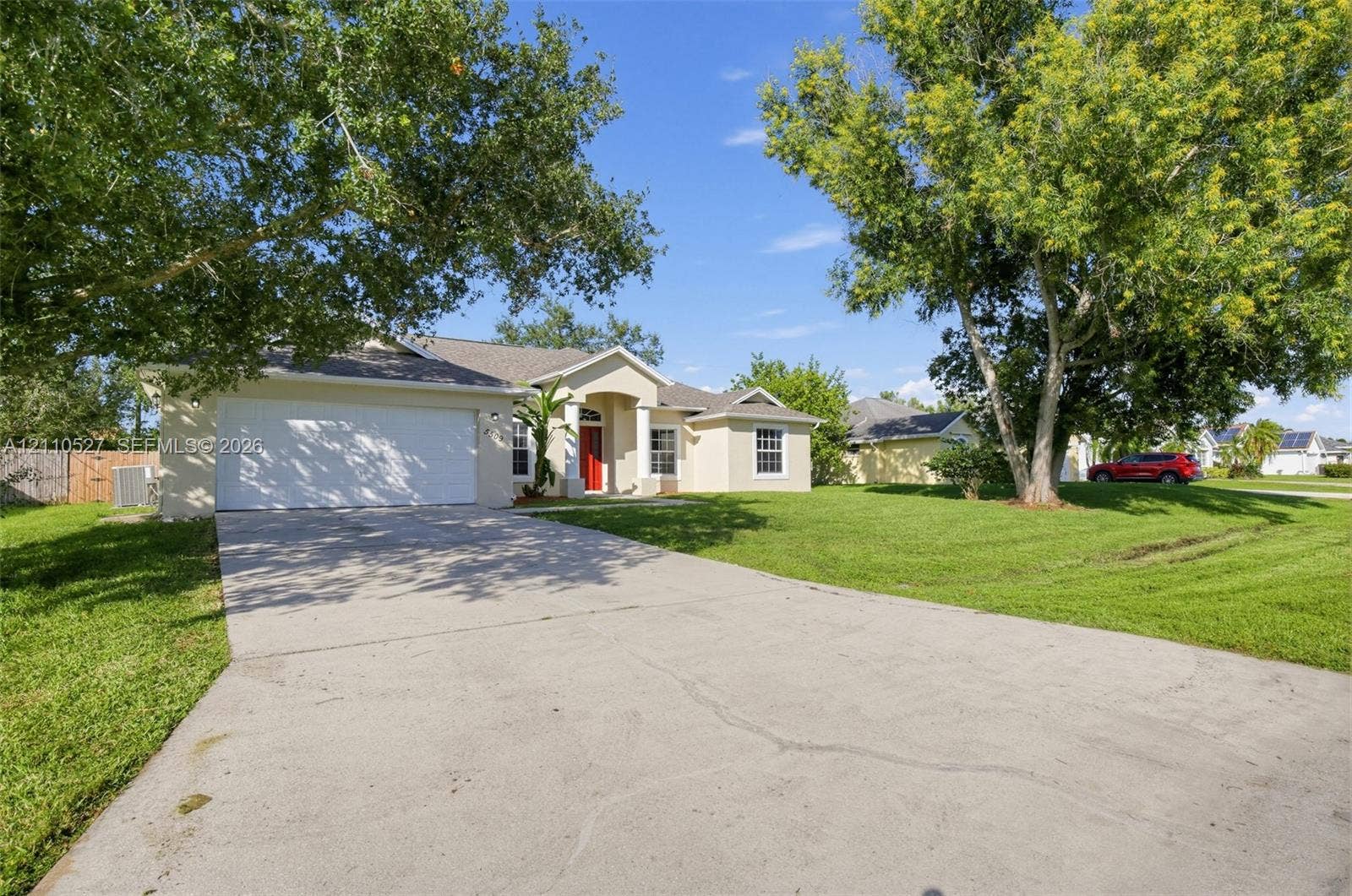 5509 NW Commodore Terrace, Port St Lucie, FL 34983 Single-story exterior featuring a stucco facade, concrete driveway, two-car garage, covered entryway with columns, and established shade trees