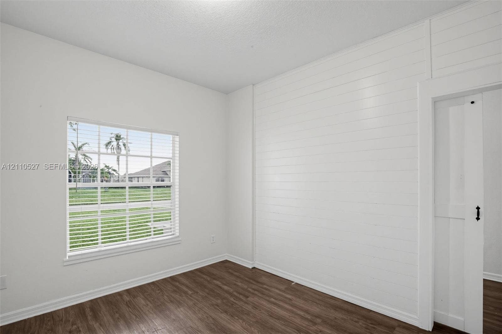 5509 NW Commodore Terrace, Port St Lucie, FL 34983 Interior space featuring wood-finish flooring, horizontal shiplap wall accent, multi-pane window with white blinds, and a white sliding door with black hardware