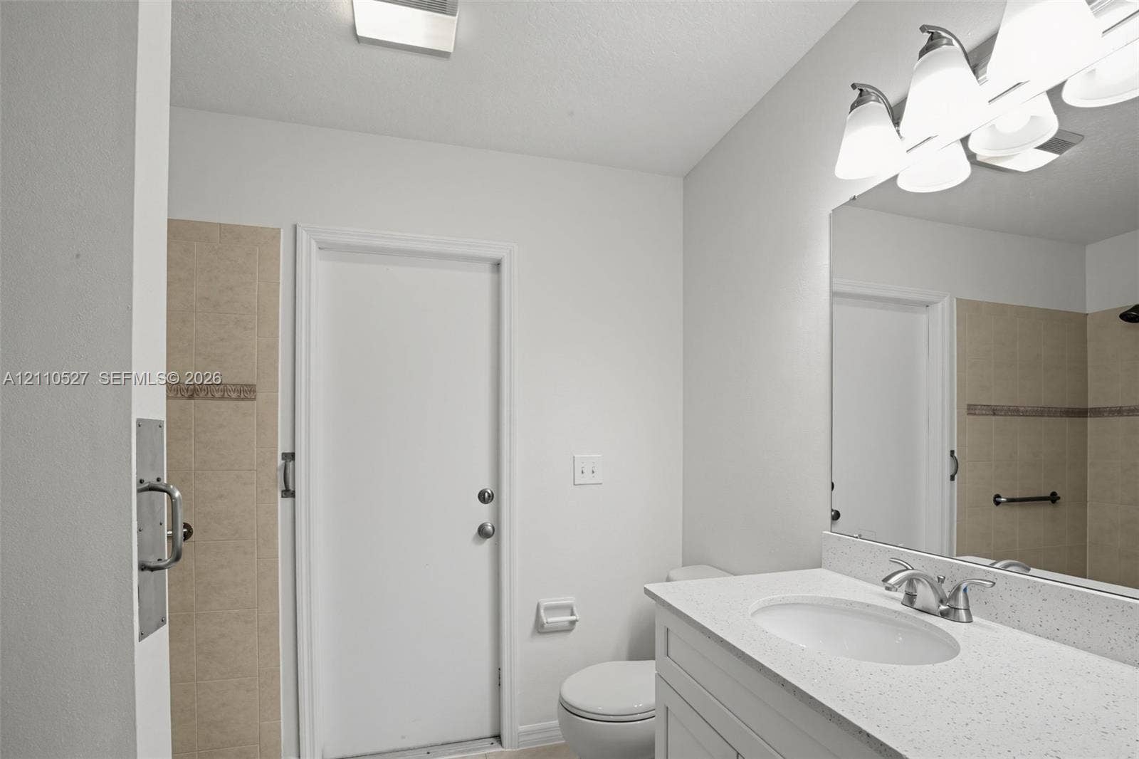 5509 NW Commodore Terrace, Port St Lucie, FL 34983 Bathroom featuring a white vanity with a quartz countertop, an integrated sink, a large wall-mounted mirror, and tile-surround shower area