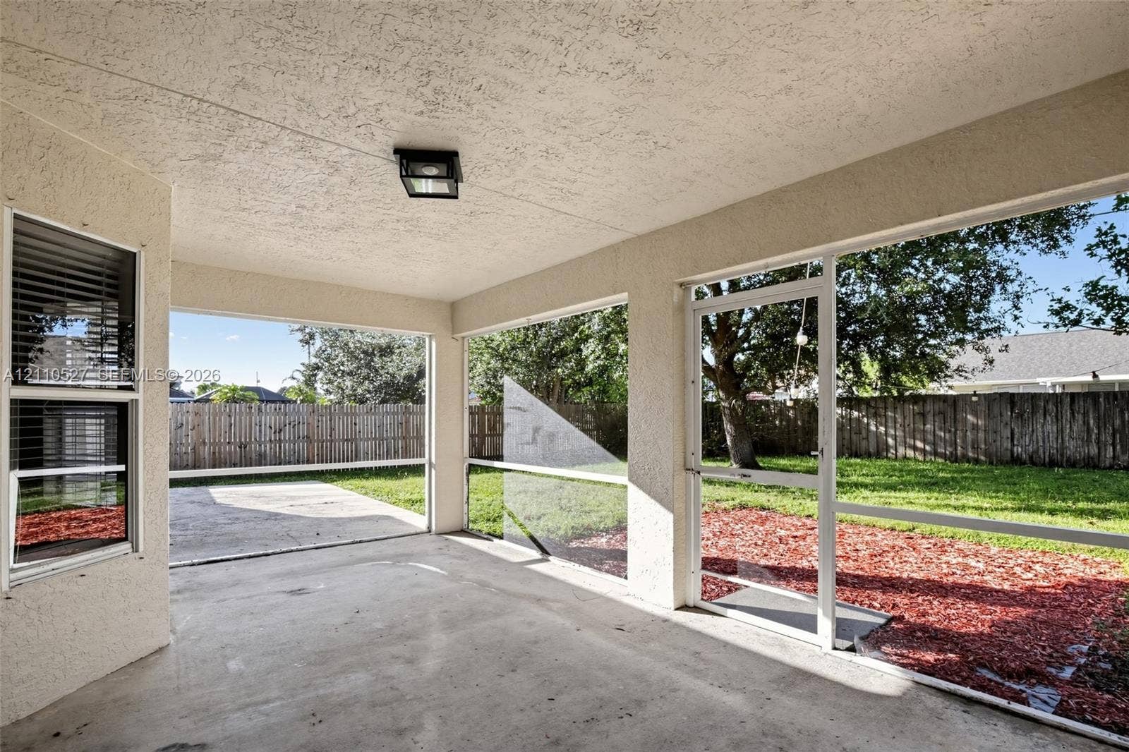 5509 NW Commodore Terrace, Port St Lucie, FL 34983 Screened-in patio with concrete flooring, stucco exterior walls, flush-mount lighting, and direct access to a fenced backyard
