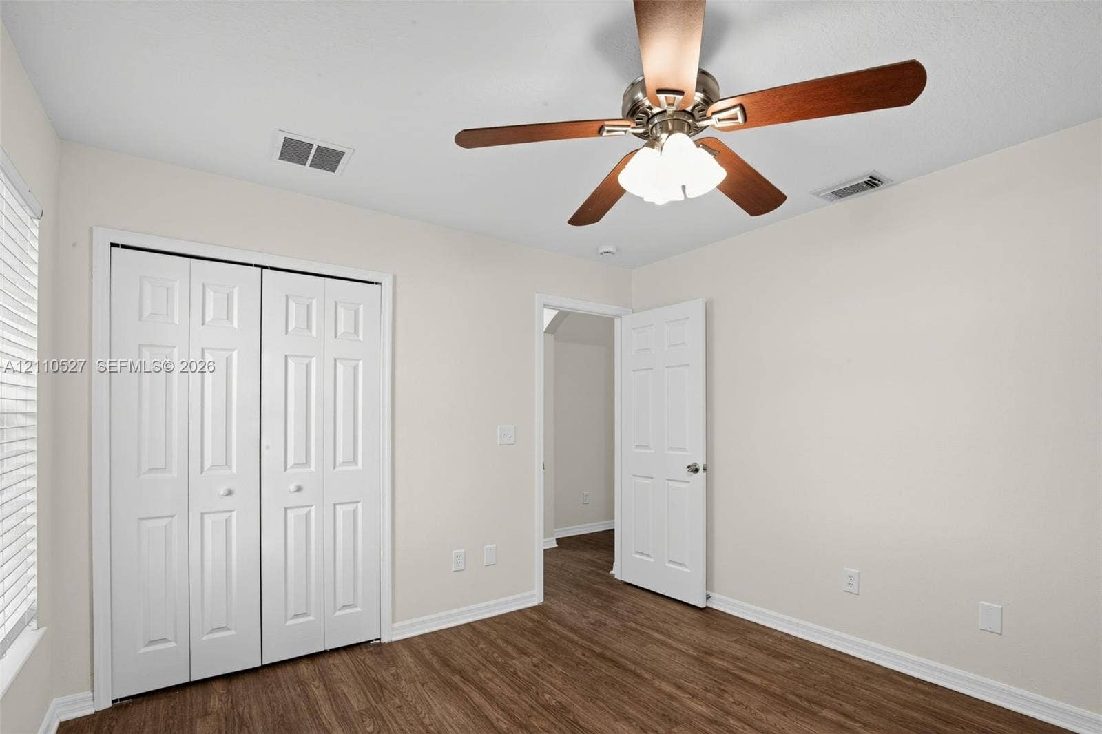 5509 NW Commodore Terrace, Port St Lucie, FL 34983 Room featuring wood-finish flooring, a ceiling fan with integrated three-bulb light fixture, and a white six-panel closet door