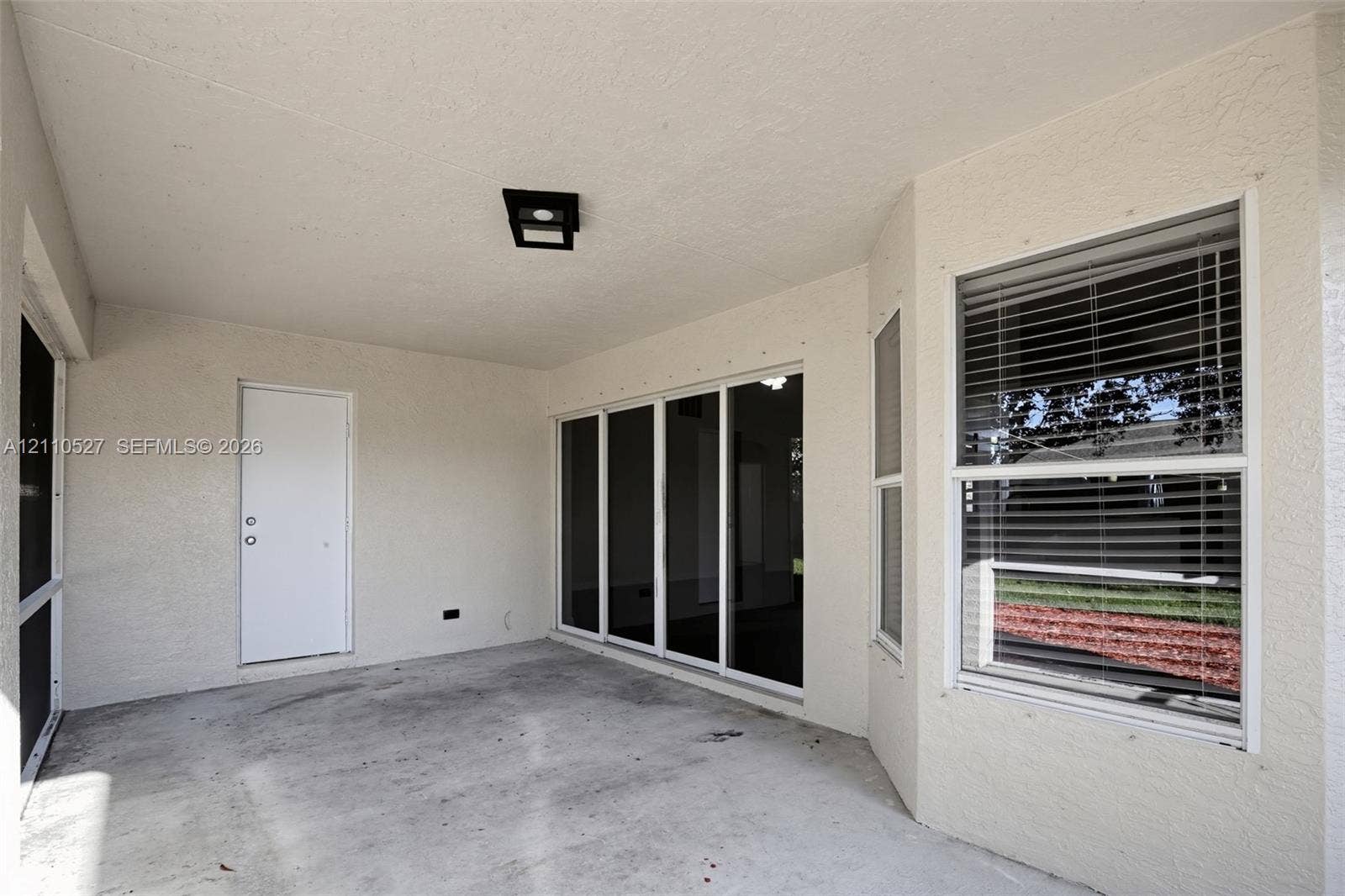 5509 NW Commodore Terrace, Port St Lucie, FL 34983 Covered patio featuring concrete flooring, multi-panel sliding glass doors, a single-panel door, and a built-in flush-mount light fixture