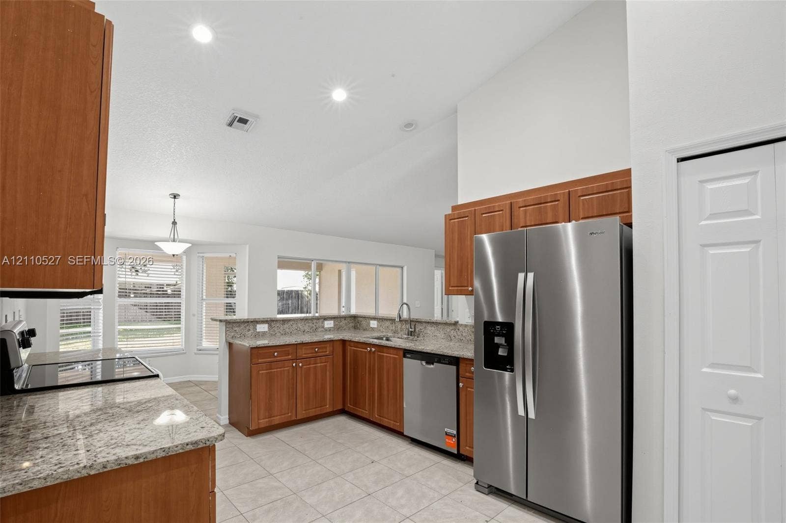 5509 NW Commodore Terrace, Port St Lucie, FL 34983 Kitchen featuring wood cabinetry, stone-finish countertops, stainless steel appliances, tile flooring, and vaulted ceilings