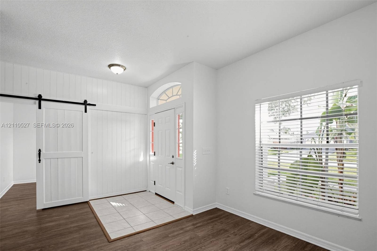 5509 NW Commodore Terrace, Port St Lucie, FL 34983 Entryway featuring vertical white wood-paneling, a sliding barn door, ceramic tile flooring, wood-finish flooring, and an arched transom window above the front door
