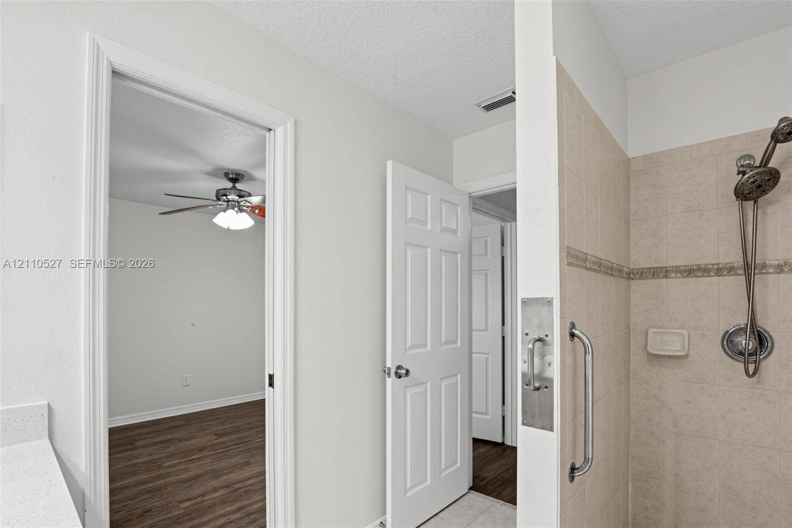 5509 NW Commodore Terrace, Port St Lucie, FL 34983 Shower stall with ceramic tile surround, handheld shower fixture, and metal grab bar, featuring a quartz-topped vanity