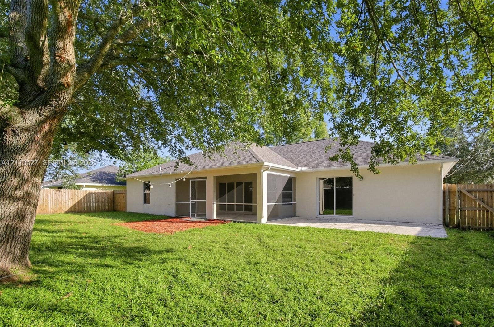 5509 NW Commodore Terrace, Port St Lucie, FL 34983 Backyard featuring a screened-in porch, concrete patio, mature trees, and wood privacy fencing