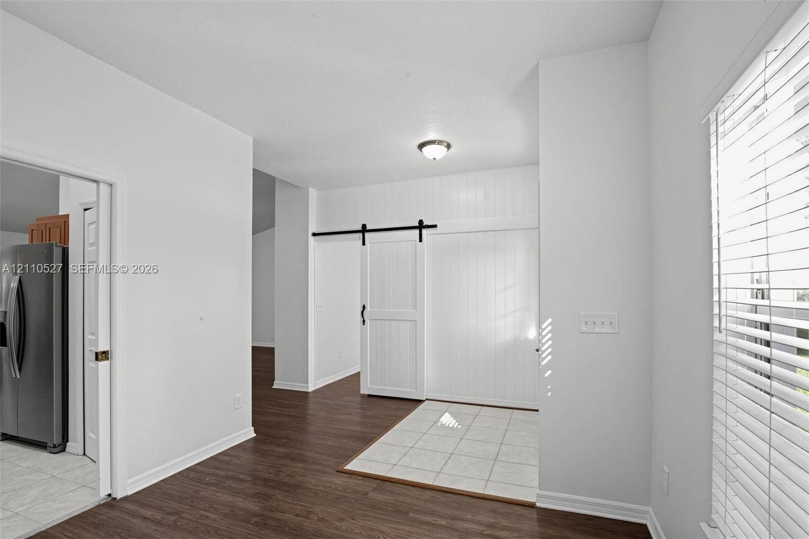 5509 NW Commodore Terrace, Port St Lucie, FL 34983 Interior featuring wood-finish flooring, white vertical-plank wall detailing, and a black metal sliding barn door