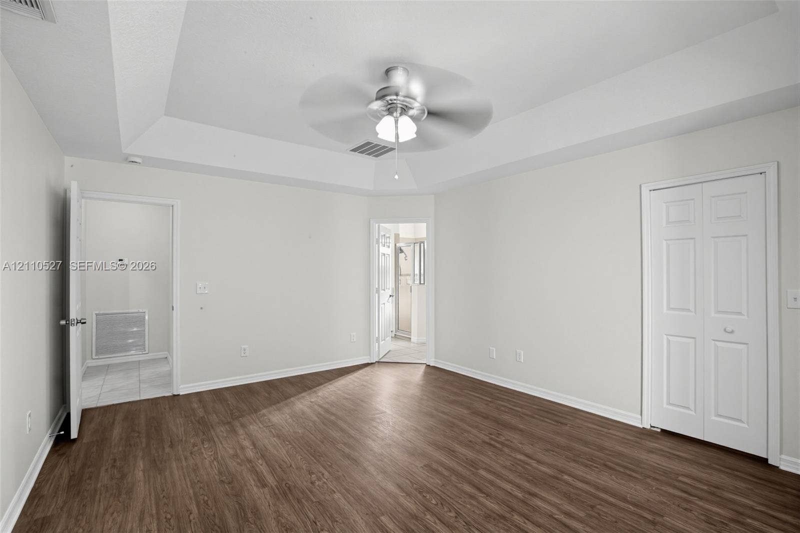 5509 NW Commodore Terrace, Port St Lucie, FL 34983 Tray ceiling featuring a central brushed-metal ceiling fan, wood-finish flooring, and white two-panel closet doors