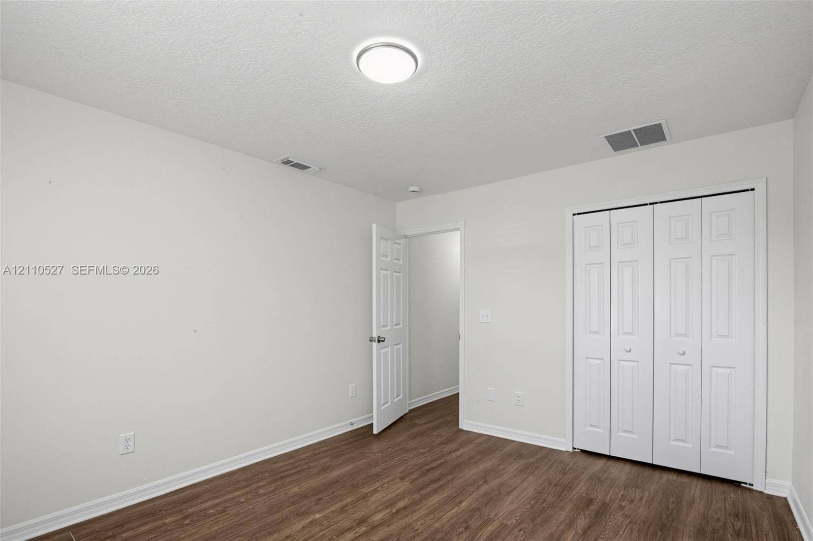 5509 NW Commodore Terrace, Port St Lucie, FL 34983 Room with neutral wall color, wood-finish flooring, white paneled interior door, and white bi-fold closet doors