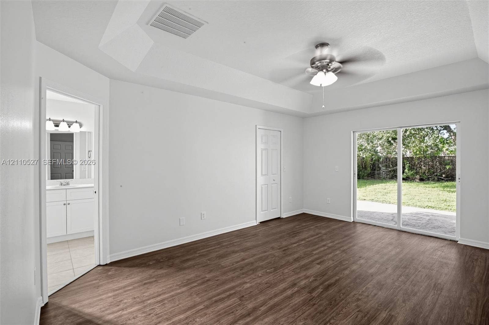 5509 NW Commodore Terrace, Port St Lucie, FL 34983 Room featuring wood-finish flooring, tray ceiling with a central ceiling fan, and sliding glass doors with exterior patio access