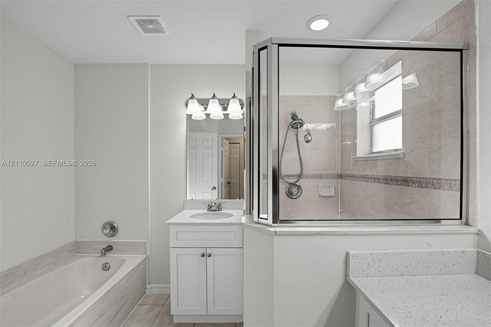 5509 NW Commodore Terrace, Port St Lucie, FL 34983 Bathroom featuring a glass-enclosed shower with tiled walls, a deep soaking tub with a tiled surround, white shaker-style cabinetry, and light-toned solid surface countertops