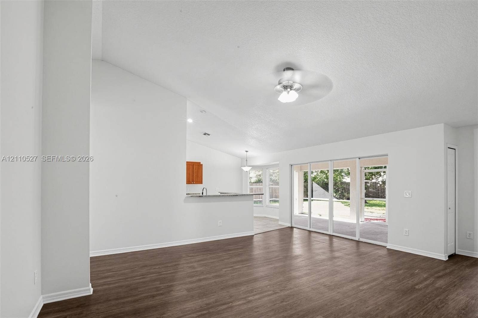 5509 NW Commodore Terrace, Port St Lucie, FL 34983 Open living area featuring vaulted ceilings, wood-finish flooring, a ceiling fan, and sliding glass doors with exterior access