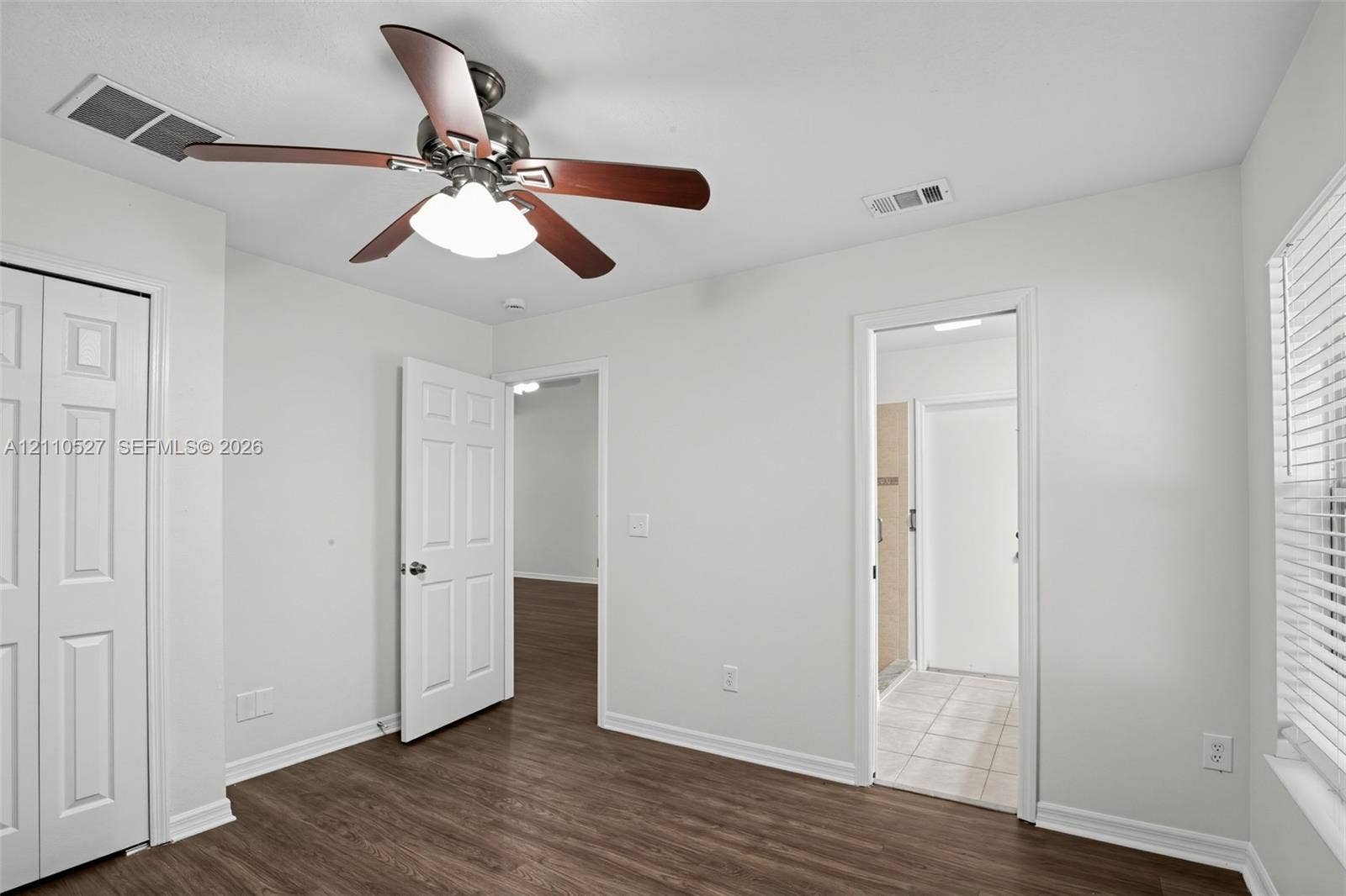 5509 NW Commodore Terrace, Port St Lucie, FL 34983 Room featuring wood-finish flooring, a multi-blade ceiling fan with integrated lighting, a six-panel closet door, and a white window with horizontal blinds