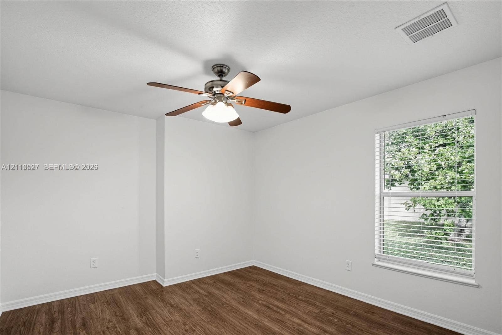 5509 NW Commodore Terrace, Port St Lucie, FL 34983 Room featuring wood-finish flooring, a neutral color palette, a ceiling fan with integrated lighting, and a window with horizontal blinds