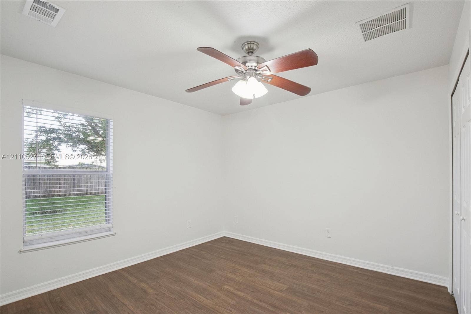 5509 NW Commodore Terrace, Port St Lucie, FL 34983 Interior space featuring wood-finish flooring, a ceiling fan with integrated lighting, and a single window with horizontal blinds