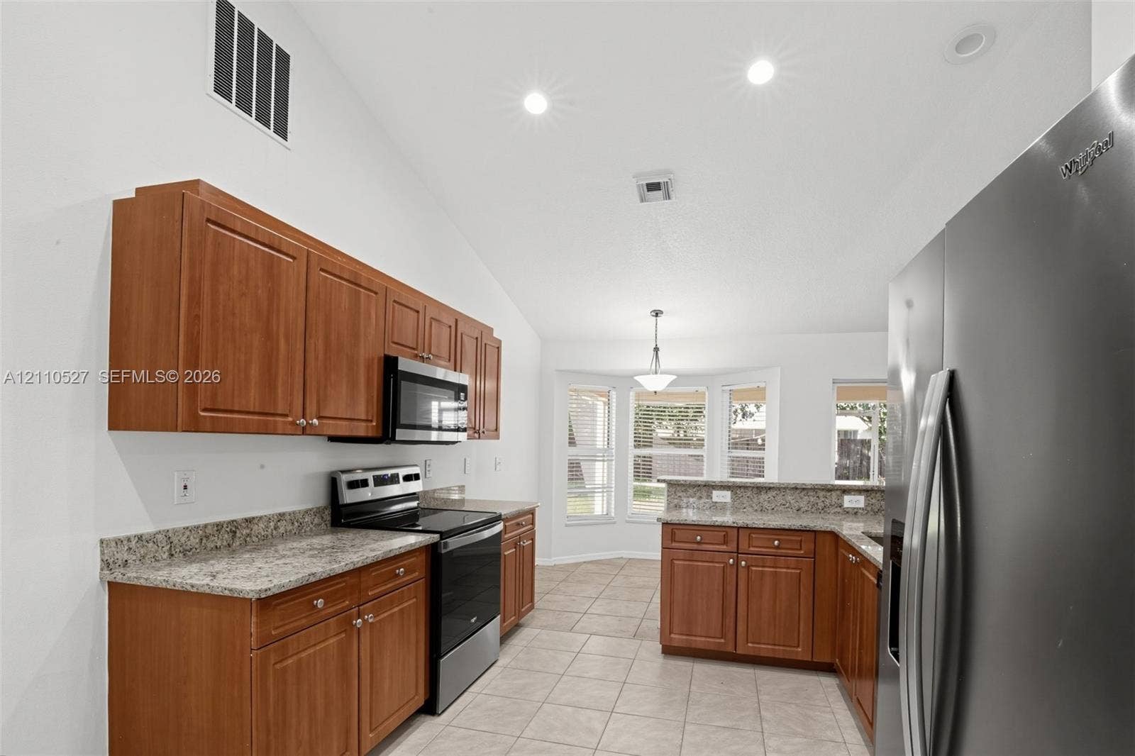 5509 NW Commodore Terrace, Port St Lucie, FL 34983 Kitchen featuring wood cabinetry, stone countertops, stainless steel appliances, tile flooring, and a vaulted ceiling