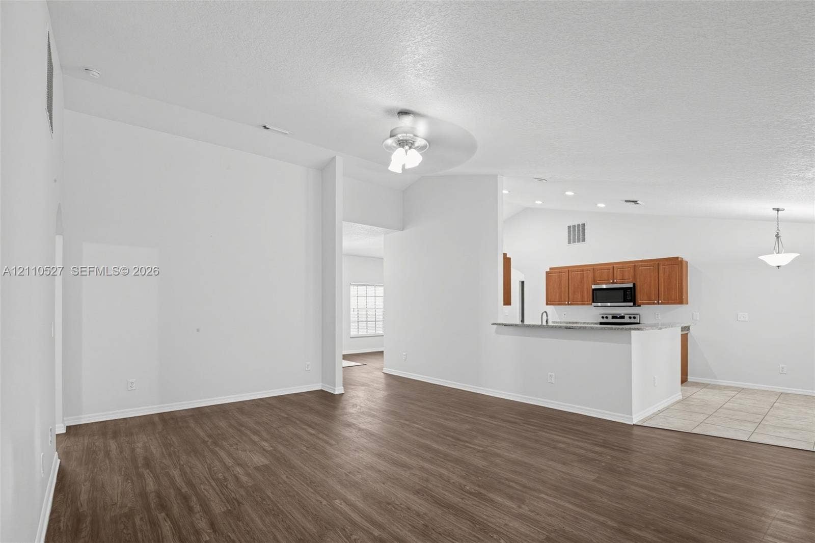 5509 NW Commodore Terrace, Port St Lucie, FL 34983 Vaulted ceilings, wood-finish flooring, kitchen featuring stone-surface countertops, wood cabinetry, and stainless steel built-in microwave