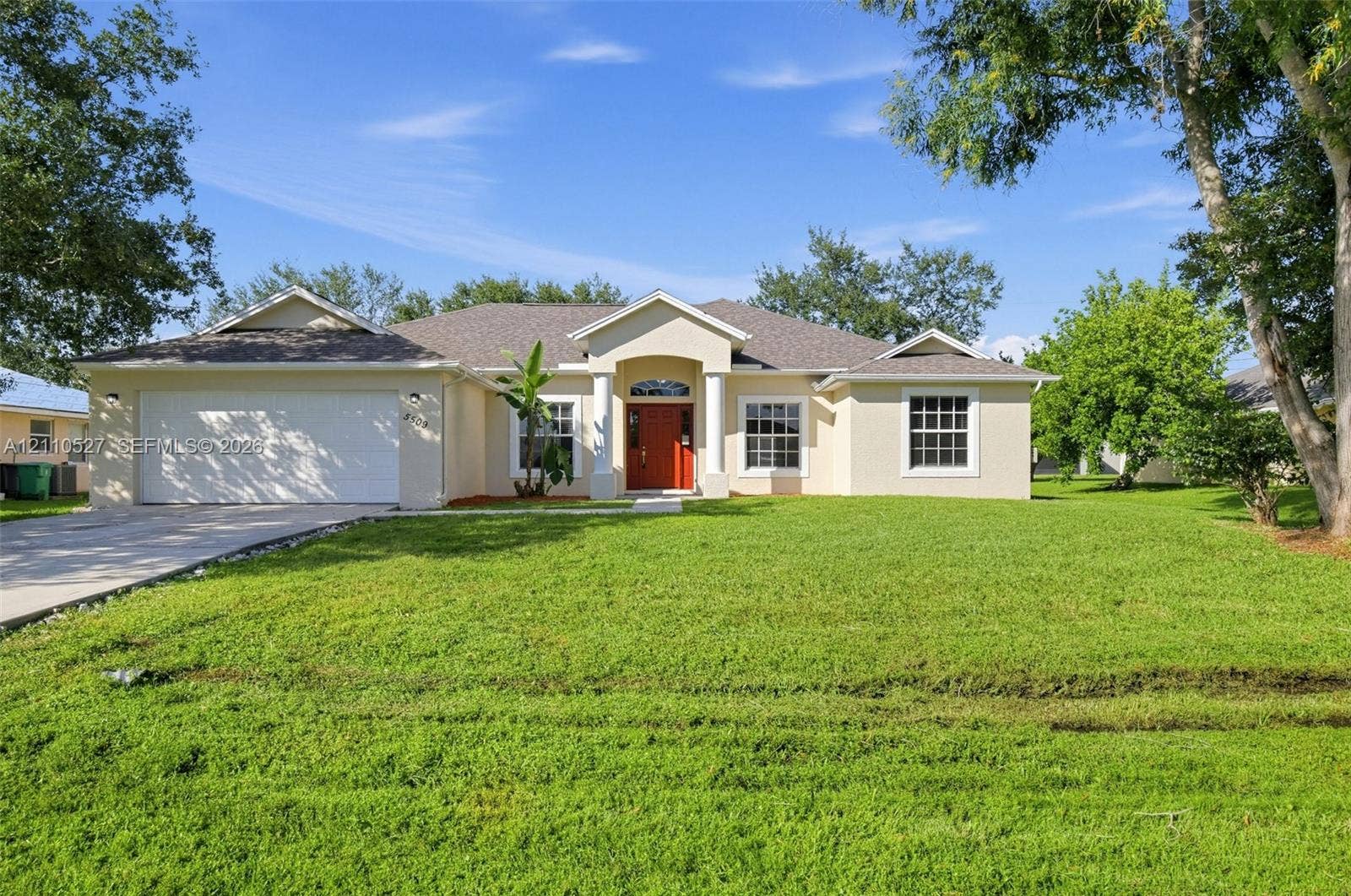 5509 NW Commodore Terrace, Port St Lucie, FL 34983 Single-story residence featuring a stucco exterior, covered entryway with arched columns, multi-pane windows, double-car garage, and mature landscaping