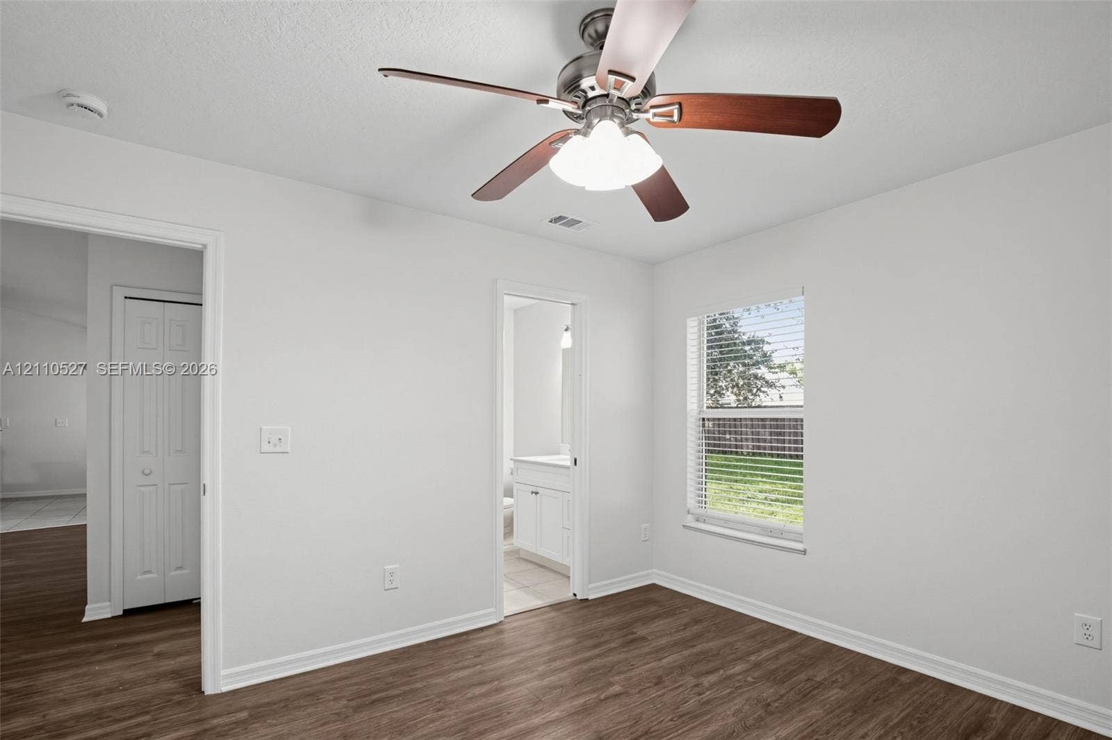 5509 NW Commodore Terrace, Port St Lucie, FL 34983 Room featuring wood-finish flooring, a multi-blade ceiling fan with integrated lighting, and a window with horizontal blinds