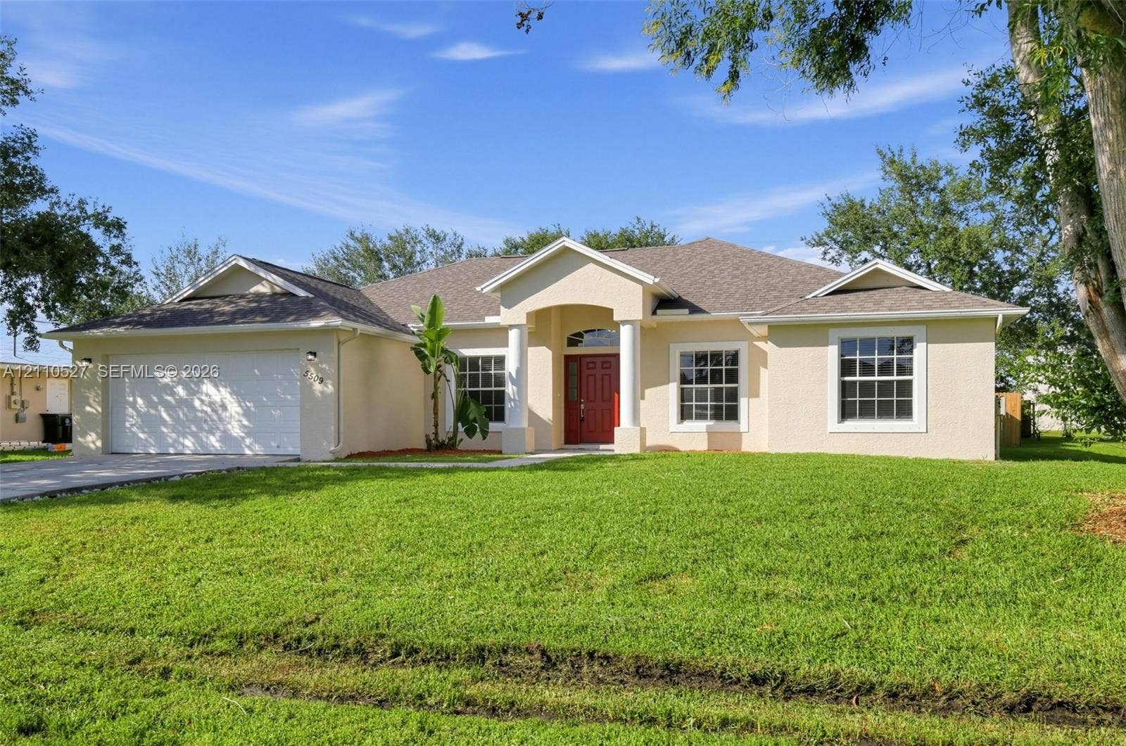 5509 NW Commodore Terrace, Port St Lucie, FL 34983 Stucco exterior residence featuring an arched entry with columns, a multi-gabled roofline, a two-car garage, and grid-pattern windows