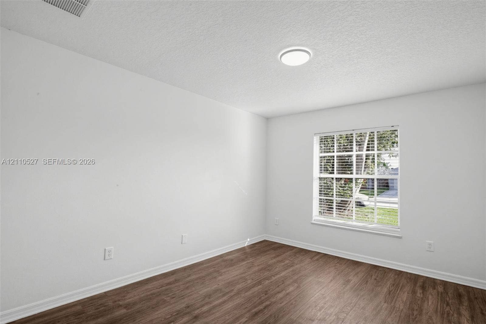 5509 NW Commodore Terrace, Port St Lucie, FL 34983 Interior room featuring wood-finish flooring, a multi-pane window, and a ceiling-mounted light fixture