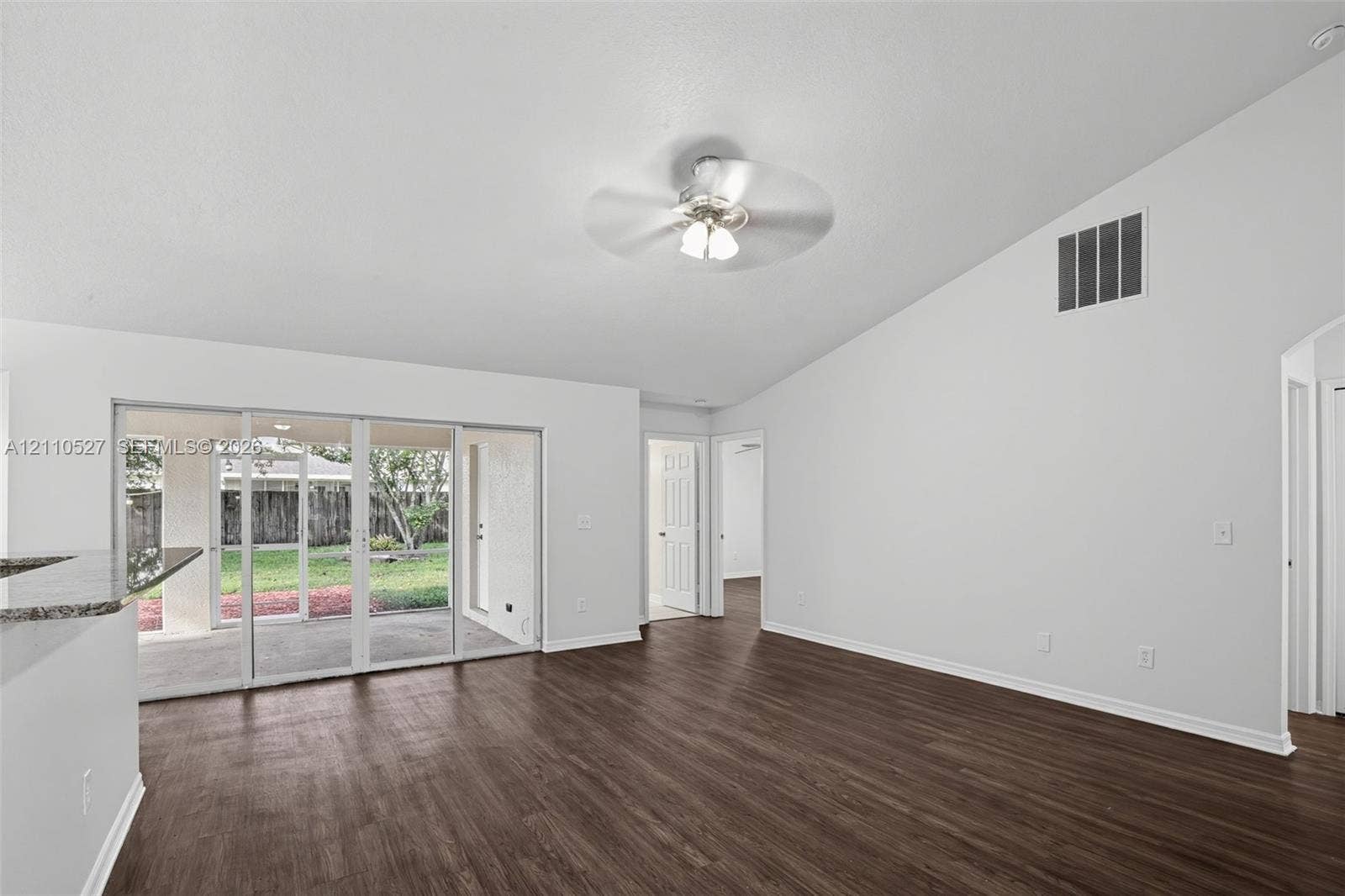 5509 NW Commodore Terrace, Port St Lucie, FL 34983 Open-concept living space featuring vaulted ceilings, wood-finish flooring, a ceiling fan with light fixture, and sliding glass doors
